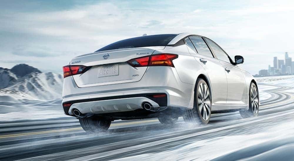 A white 2021 Nissan Altima is driving through the snow.