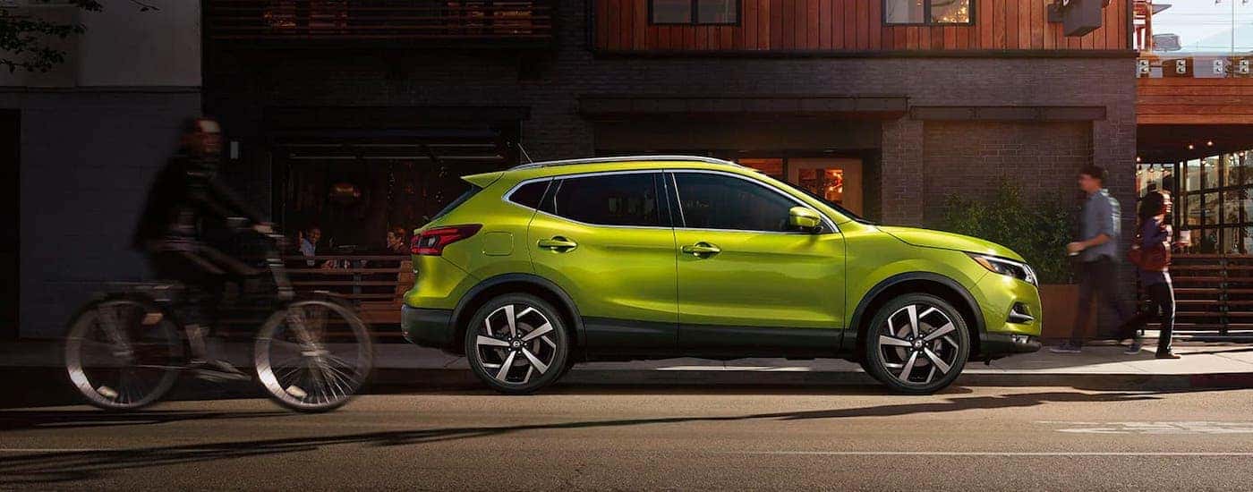 A green 2021 Nissan Rogue Sport is shown from the side while parked on a city street.