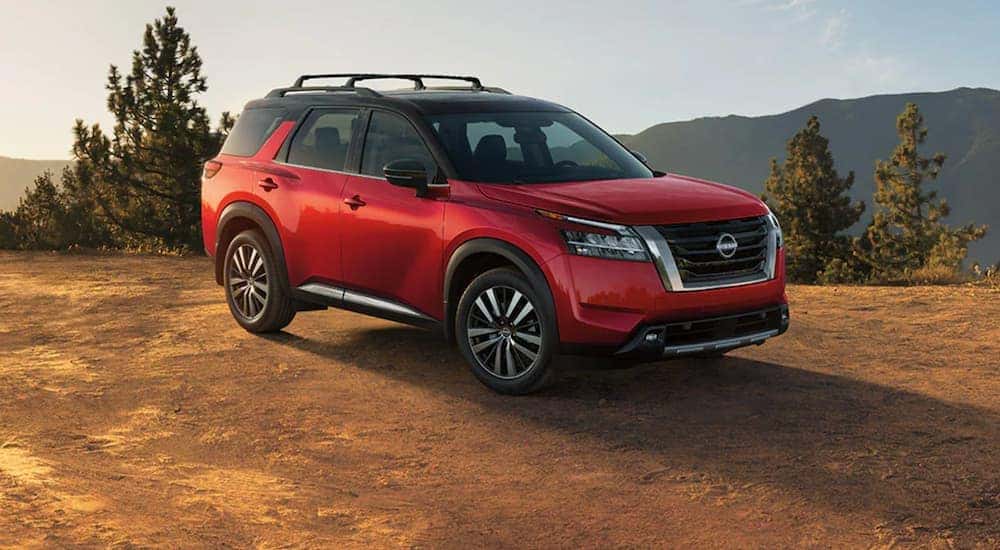 A red 2022 Nissan Pathfinder is shown from the side parked on dirt after looking at new cars in stock.