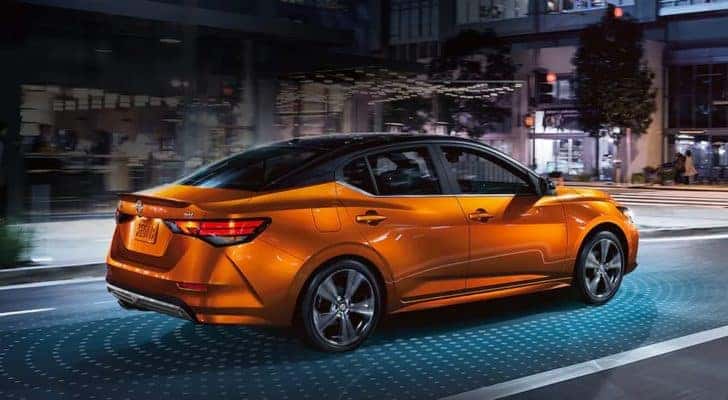 An orange 2021 Nissan Sentra is shown driving in a city at night.