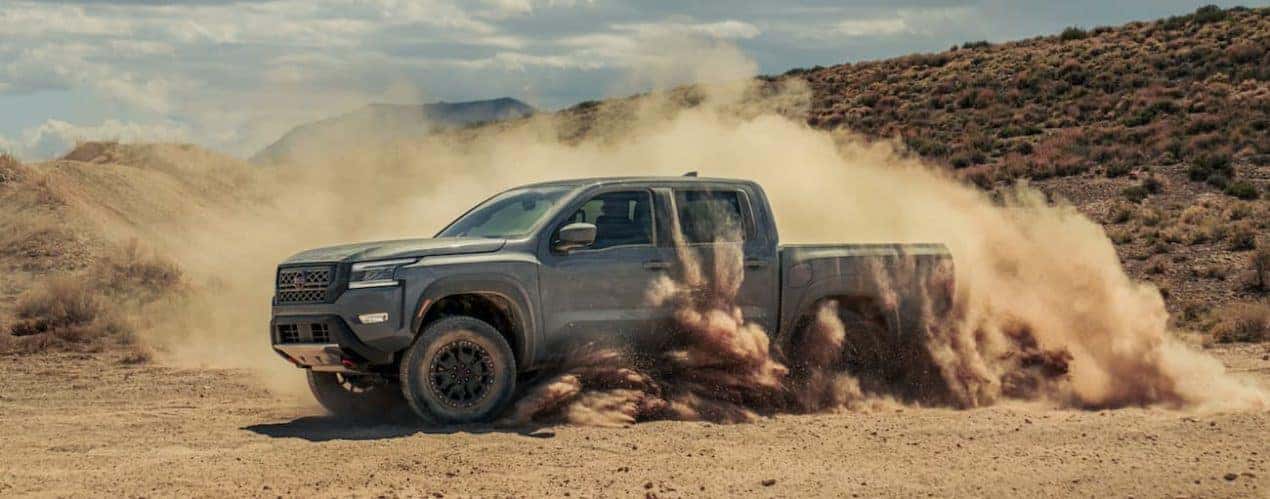 A grey 2022 Nissan Frontier is shown from the side off-roading in the desert.