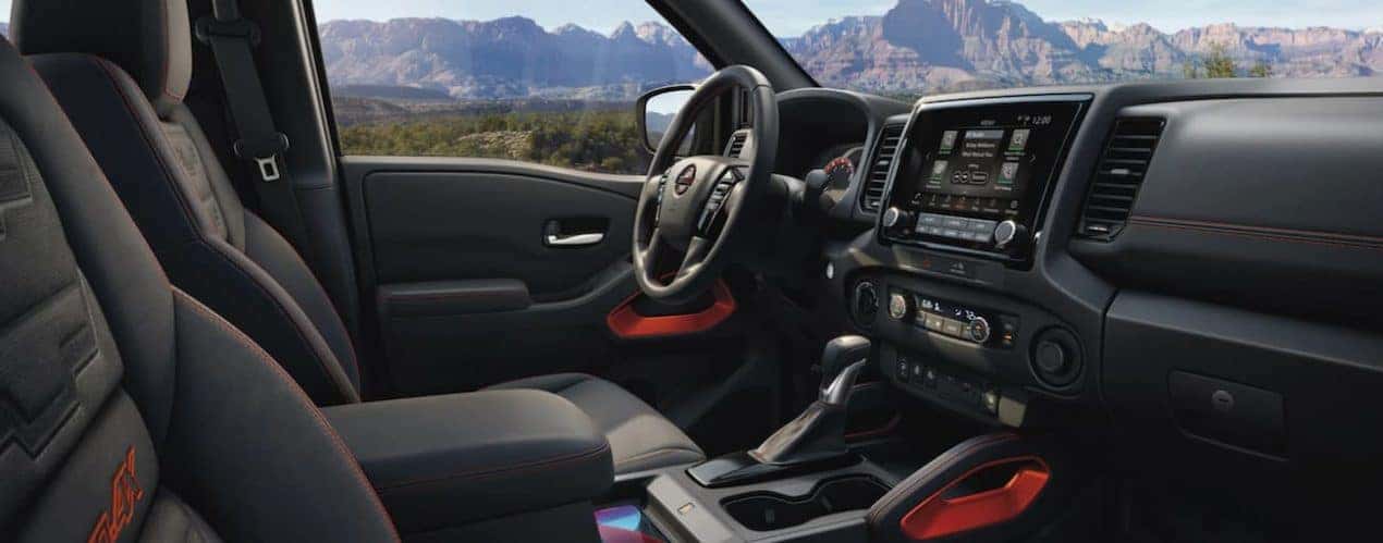 The black interior of a 2022 Nissan Frontier shows the steering wheel and infotainment screen.