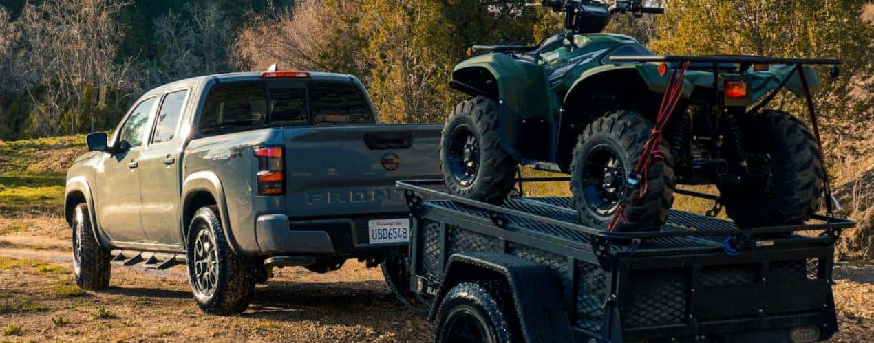 A grey 2022 Nissan Frontier is shown towing a trailer carrying an ATV during a 2022 Nissan Frontier vs 2022 Chevy Colorado comparison.