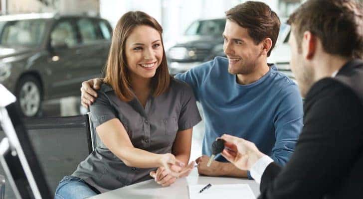 A couple is shown talking to a salesperson at a certified pre-owned dealership.