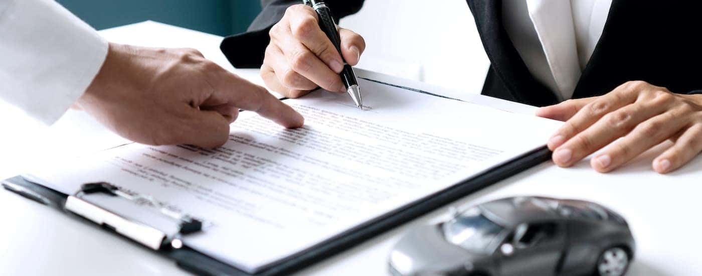 A person is shown signing paperwork at a car dealership.
