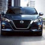 A blue 2020 Nissan Altima is shown from the front driving through a city.