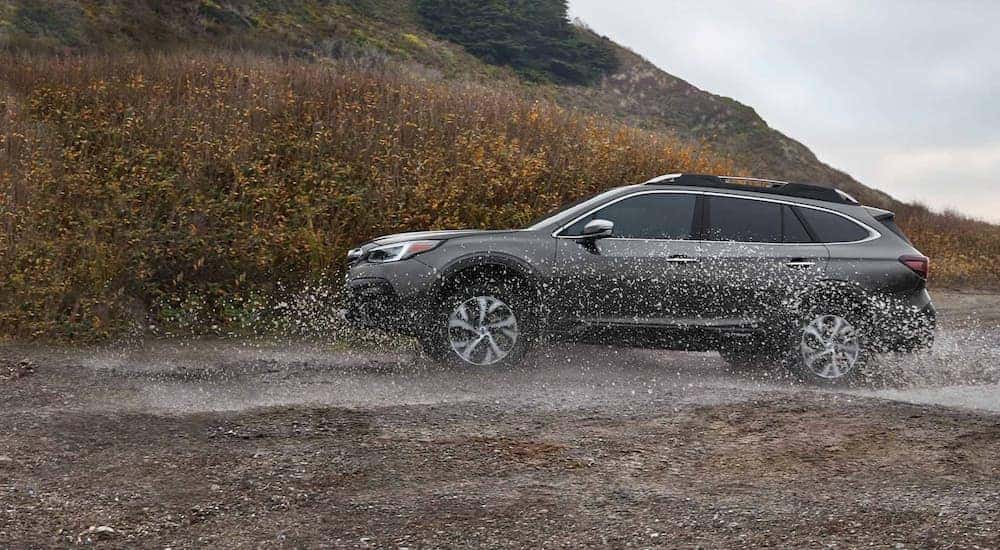 A grey 2021 Subaru Outback is shown from the side while it drives through mud.