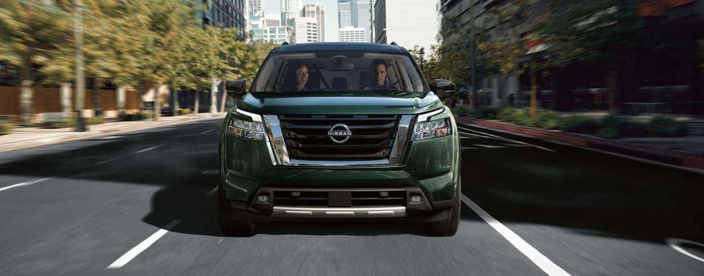 A green 2022 Nissan Pathfinder is shown from the front driving on an open road through a city after leaving a Nissan SUV dealer.