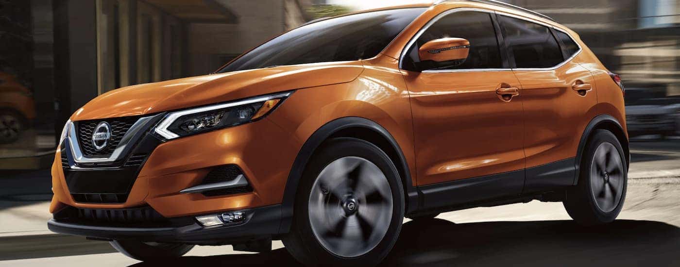 An orange 2022 Nissan Rogue Sport is shown from the side driving through a city.