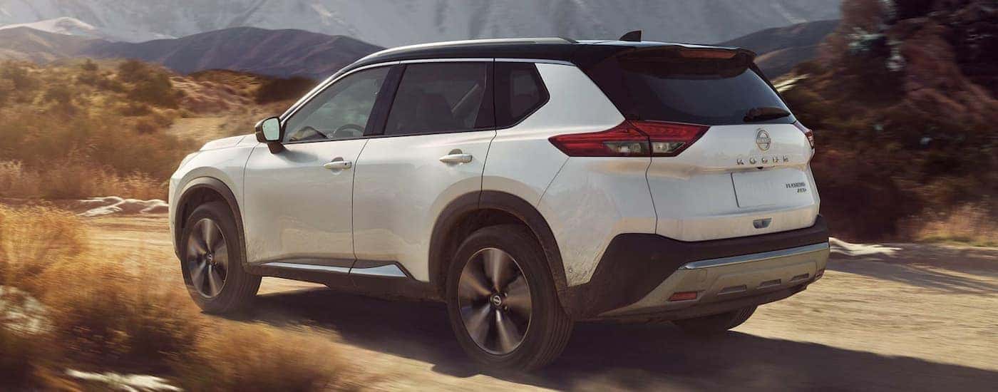 A white 2022 Nissan Rogue is shown from the rear driving on a dirt road.