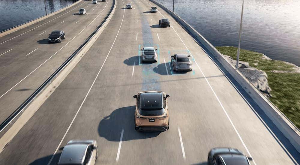 A gold 2023 Nissan ARIYA is shown from a high angle driving on a busy highway.