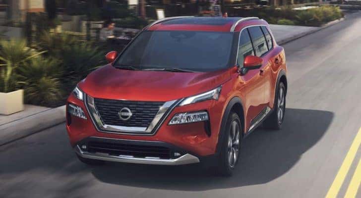 A red 2023 Nissan Rogue is shown from the front driving on an open road.