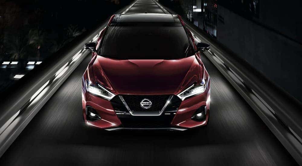 A maroon 2021 Nissan Maxima driving on an illuminated street at night