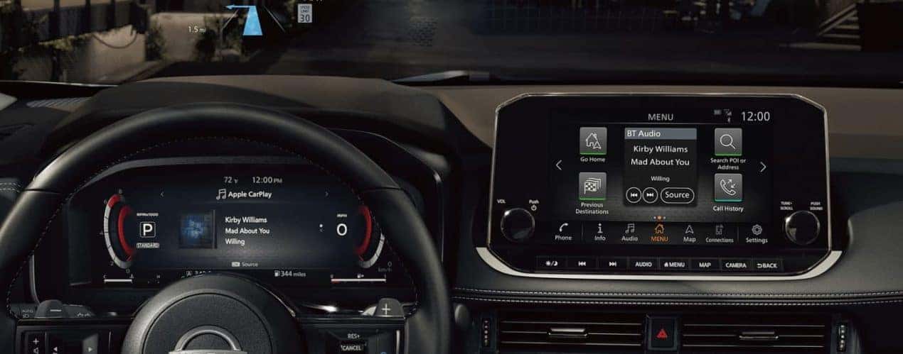 The black interior of a 2023 Nissan Rogue shows the steering wheel and infotainment screen.