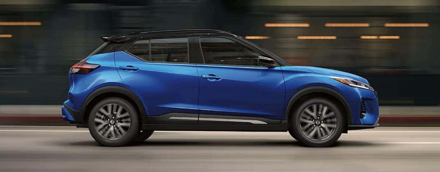 A blue 2021 Nissan Kicks is shown from the side driving to a certified Nissan Kicks dealer.