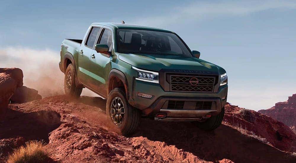 A green 2023 Nissan Frontier PRO-4x off-roading on a dusty dirt trail.