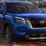 Front view of a blue 2023 Nissan Pathfinder towing an ATV on a dusty dirt road