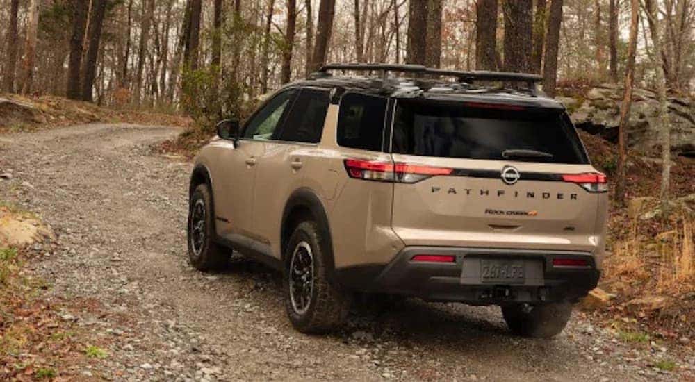 Rear view of a tan Nissan Pathfinder driving up a rocky trail in the woods