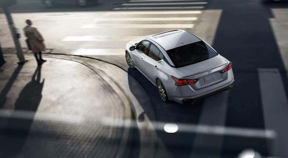 Aerial view of a white 2023 Nissan Altima SR taking a left turn through a city intersection.