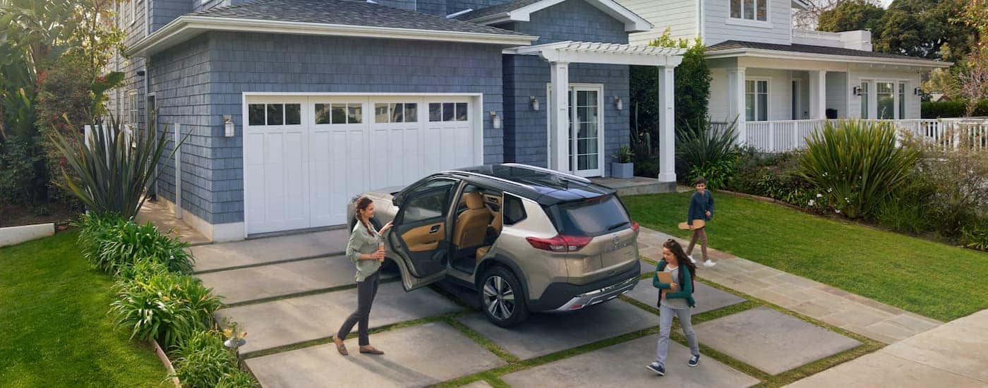 A family is shown standing around a tan 2022 Nissan Rogue Platinum.