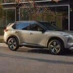 A woman crosses the street after parking her silver 2023 Nissan Rogue Platinum AWD in front of an office building
