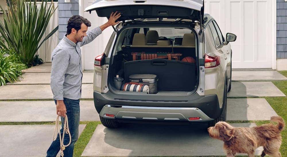 A man is shown opening the liftgate of a tan 2023 Nissan Rogue for a dog.