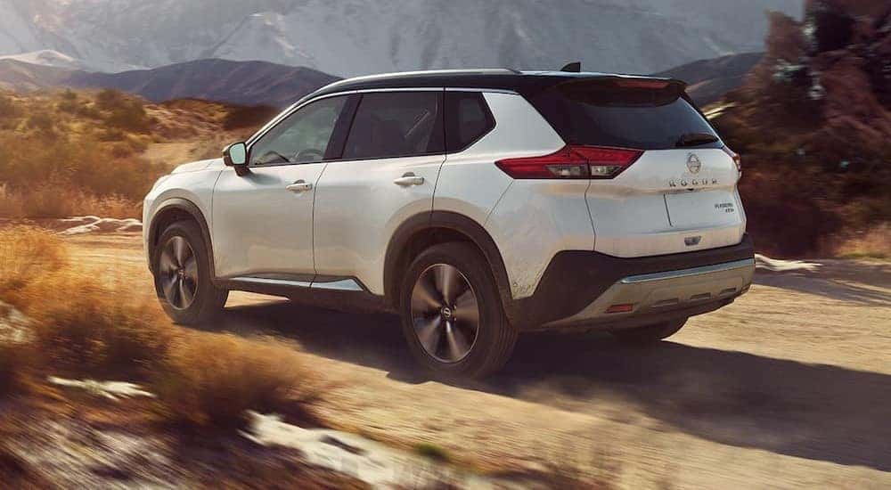 A white 2023 Nissan Rogue is shown off-roading on a dirt path in the mountains.
