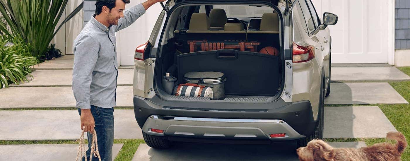A man is shown closing the rear liftgate on a tan 2023 Nissan Rogue Platinum.