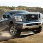 A grey 2024 Nissan Titan for sale is shown driving off-road.