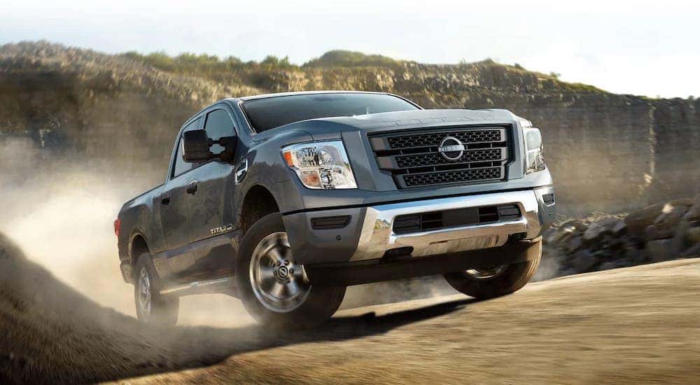 A grey 2024 Nissan Titan for sale is shown driving off-road.