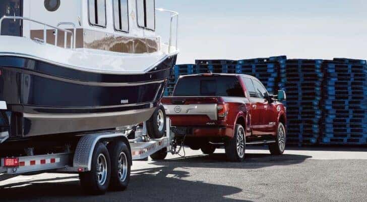 A red 2023 Nissan Titan is shown from the rear at an angle while towing a boat.