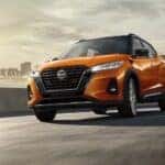 An orange 2024 Nissan Kicks for sale near Columbia is shown driving from a city.