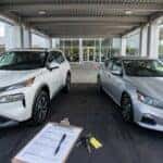 Pre-owned Nissan Rogue and Altima under a dealership delivery canopy with an inspection checklist