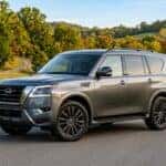 A clean commercial photograph of a 2025 Nissan Armada full-size SUV featuring factory 22-inch alloy wheels, parked at a three-quarter front angle along a paved access road in a Middle Tennessee suburban park, late afternoon golden hour lighting highlighting the metallic dark grey paint and sleek body lines, surrounding landscape of gently rolling hills with early fall foliage showing subtle touches of yellow and orange amidst rich green oak trees, realistic automotive lifestyle imagery, crisp depth of field with soft park background, no license plate. No text, no logos other than natural vehicle badging, no identifiable faces. (Representative image for illustration purposes only. Actual vehicle may vary based on trim and configuration.)