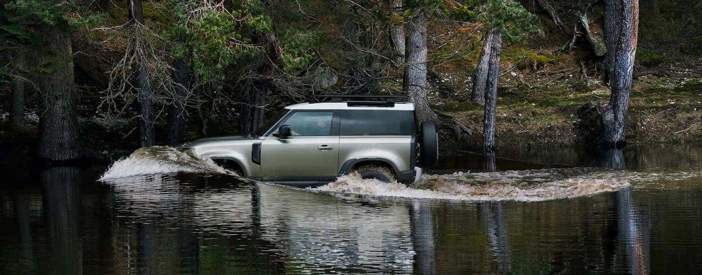 A green 2025 Land Rover Defender is shown from the side while crossing a river.