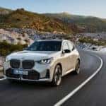 A tan 2025 BMW X3 M50 is shown from the front after leaving a BMW dealer.