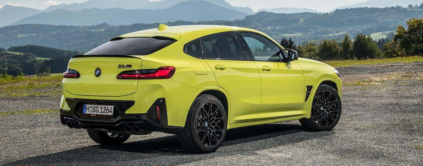 A yellow 2025 BMW X4M is shown from the rear at an angle.