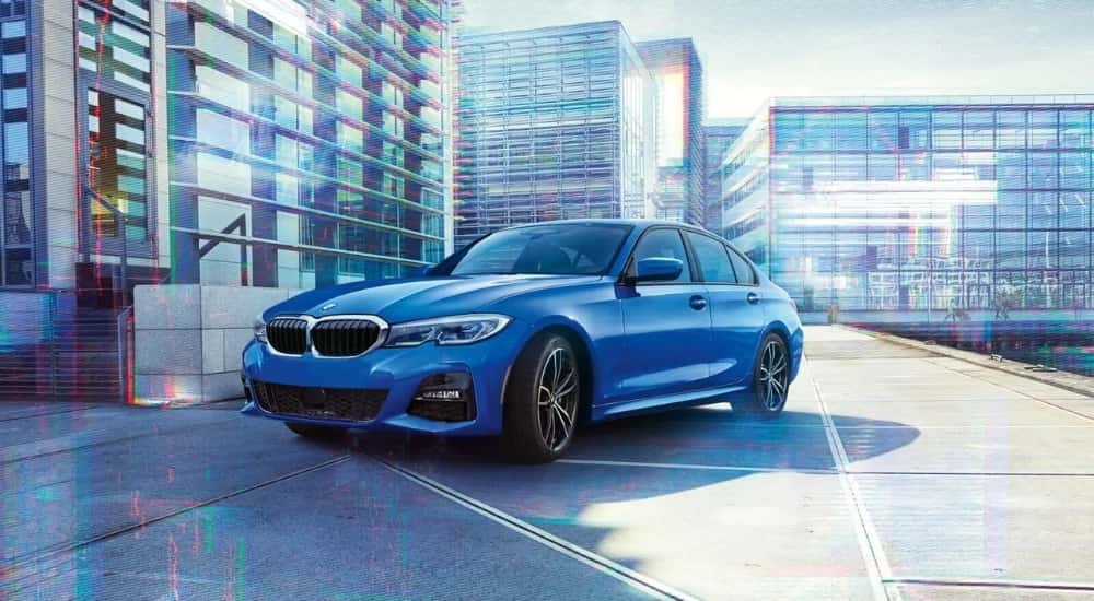 A blue 2020 BMW 330i is shown parked near buildings.