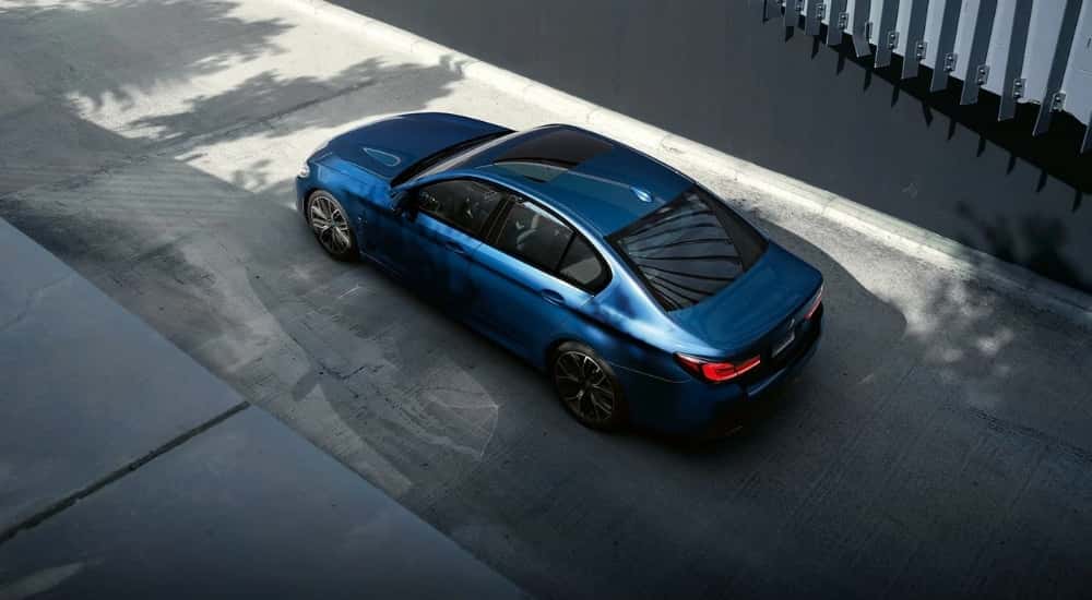 A blue 2023 BMW 530e is shown from a high angle in an alleyway.