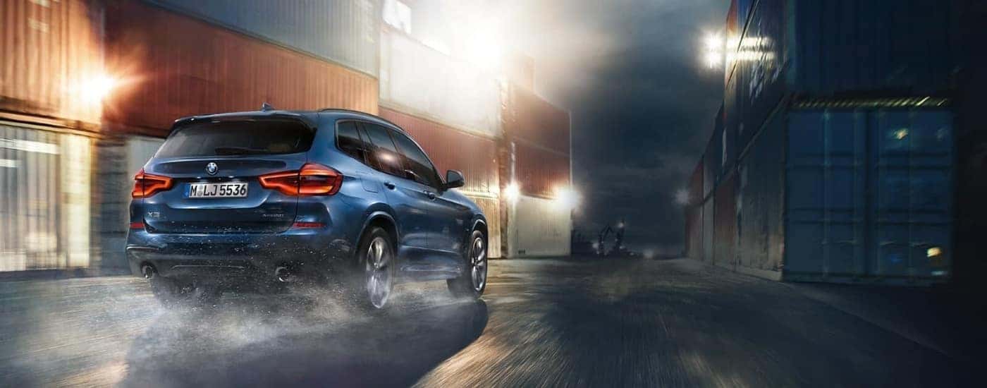 A blue 2018 BMW X3 driving past shipping containers.