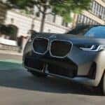 A gray 2025 BMW X3for sale driving in a city.