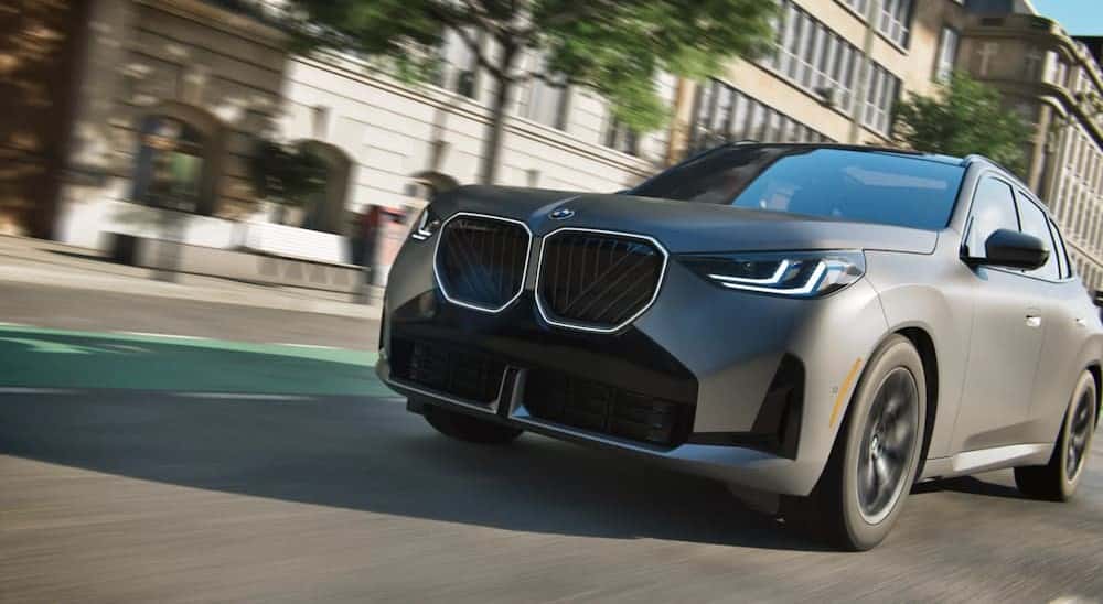 A gray 2025 BMW X3for sale driving in a city.