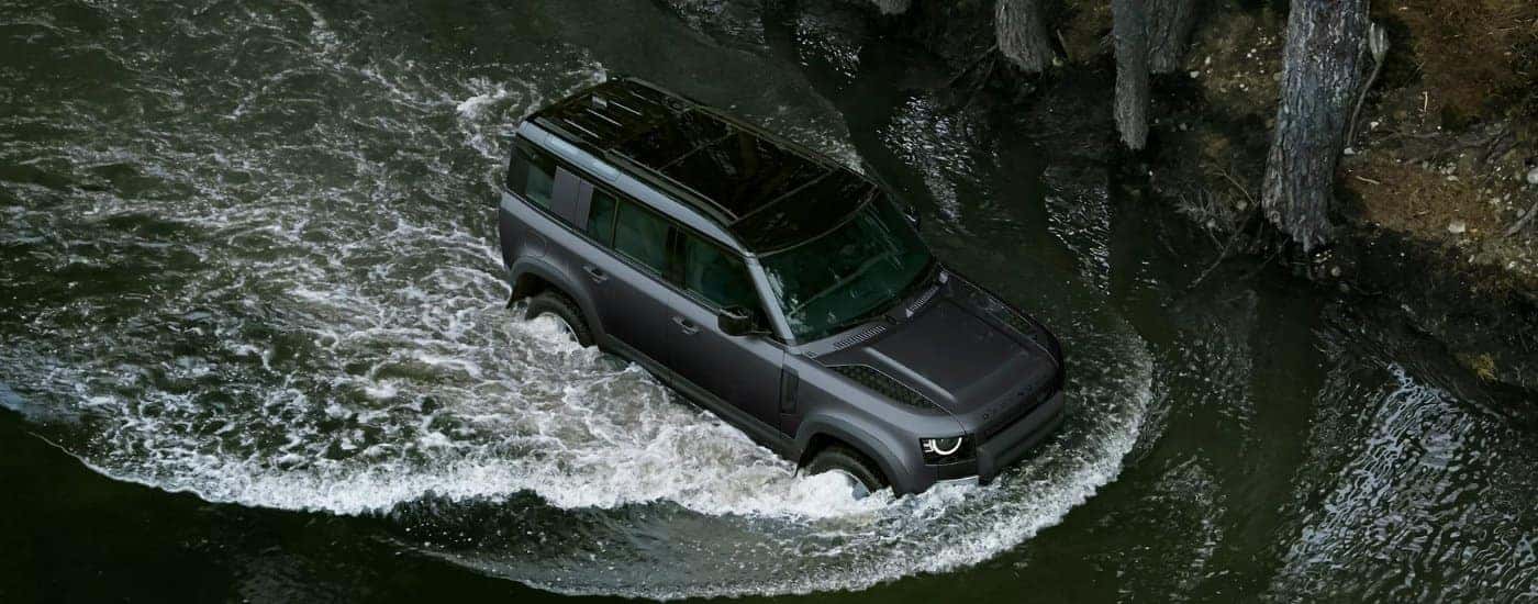 A grey 2025 Land Rover Defender 110 driving through a creek to a Land Rover dealer.
