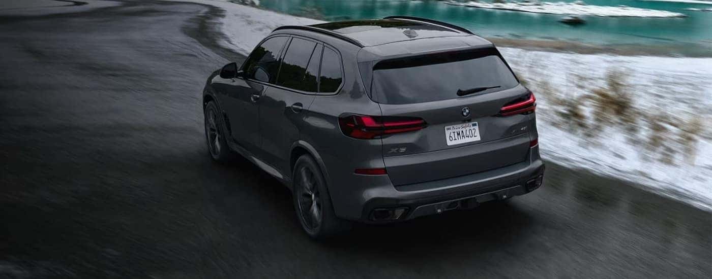 A grey 2024 BMW X5 driving past a river.