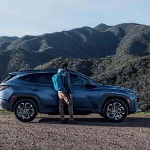 the exterior of a blue suv parked on gravel next to a forest