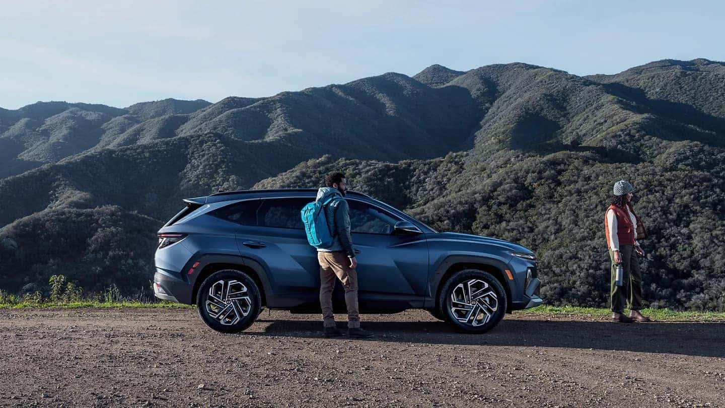 the exterior of a blue suv parked on gravel next to a forest