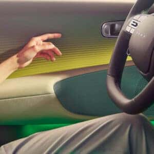 A close-up of a person interacting with the Hyundai Ioniq 6’s door panel, featuring green and yellow ambient lighting.