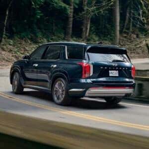 Rear view of the 2023 Hyundai Palisade driving through a forested road.