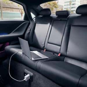 Black leather rear seats of the Hyundai Ioniq 6 with ambient lighting, featuring a laptop plugged into the car’s power outlet.