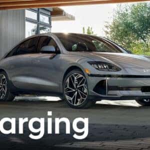 A Hyundai IONIQ 6 charging in a modern home garage, plugged into an EV charging station. Text overlay reads 